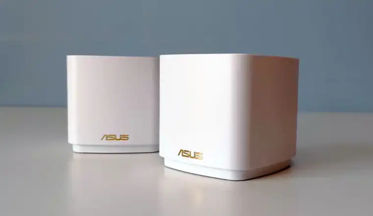 Two white ASUS ZenWiFi AX Mini (XD5) routers on white surface.