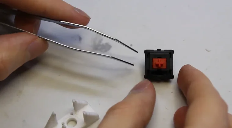 A mechanical switch on a table with hands holding a keycap puller nearby