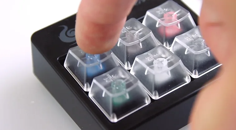 Six mechanical keyboard switches arranged together with a finger pressing one of them
