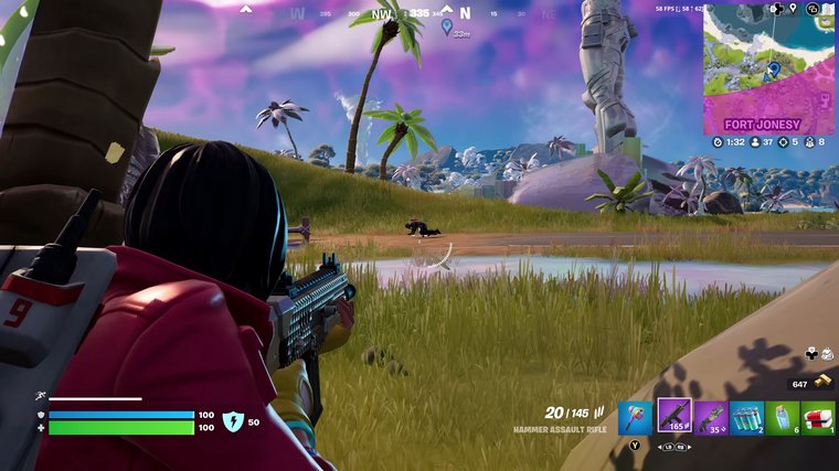 Fortnite - aiming at an enemy player who is on the ground crouching in an open field near a body of water.