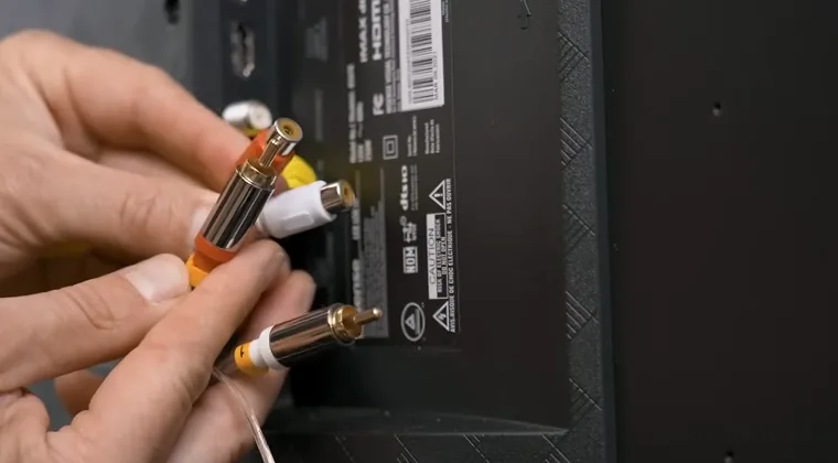 Back of a TV with RCA and AUX cables held in a person’s hand