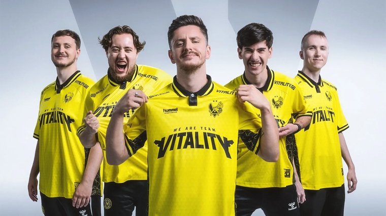 Team Vitality’s Counter-Strike 2 squad posing together, tugging on their shirts and smiling excitedly at the camera.