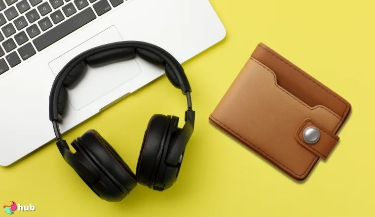 Black over-ear headphones next to a laptop and a brown leather wallet on a yellow background