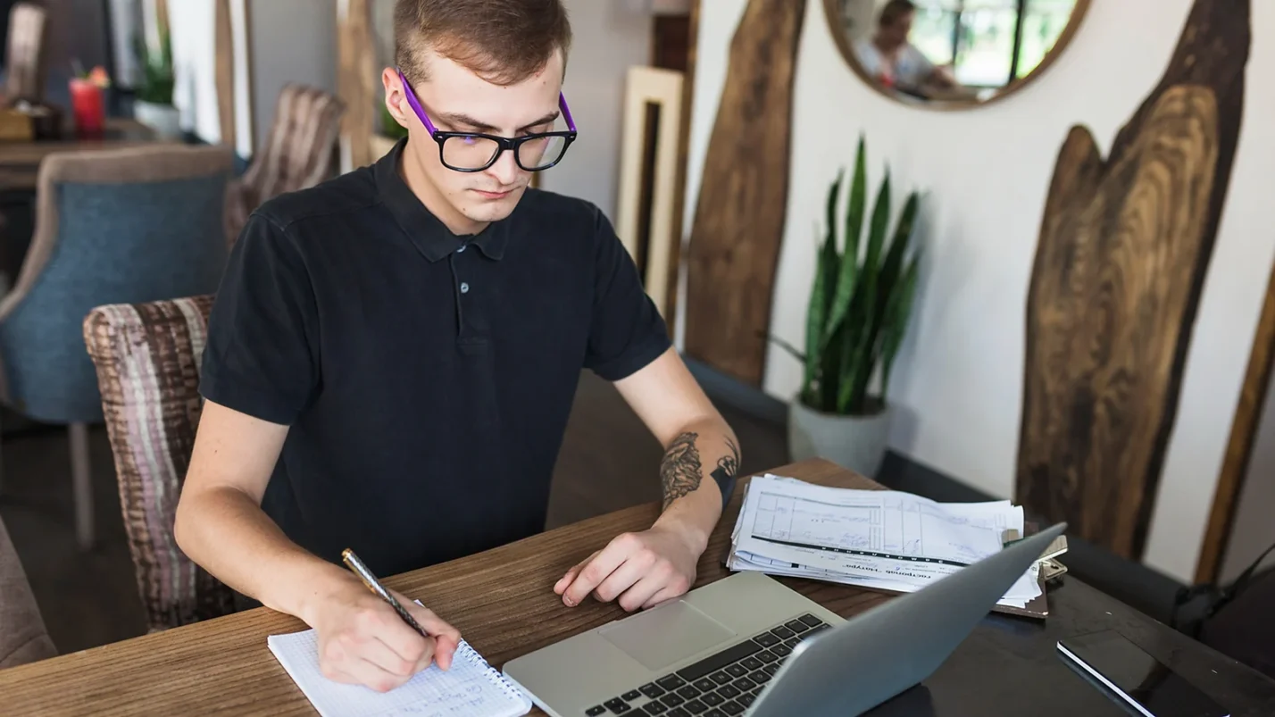 Man sitting in front of laptop and writing something on the paper