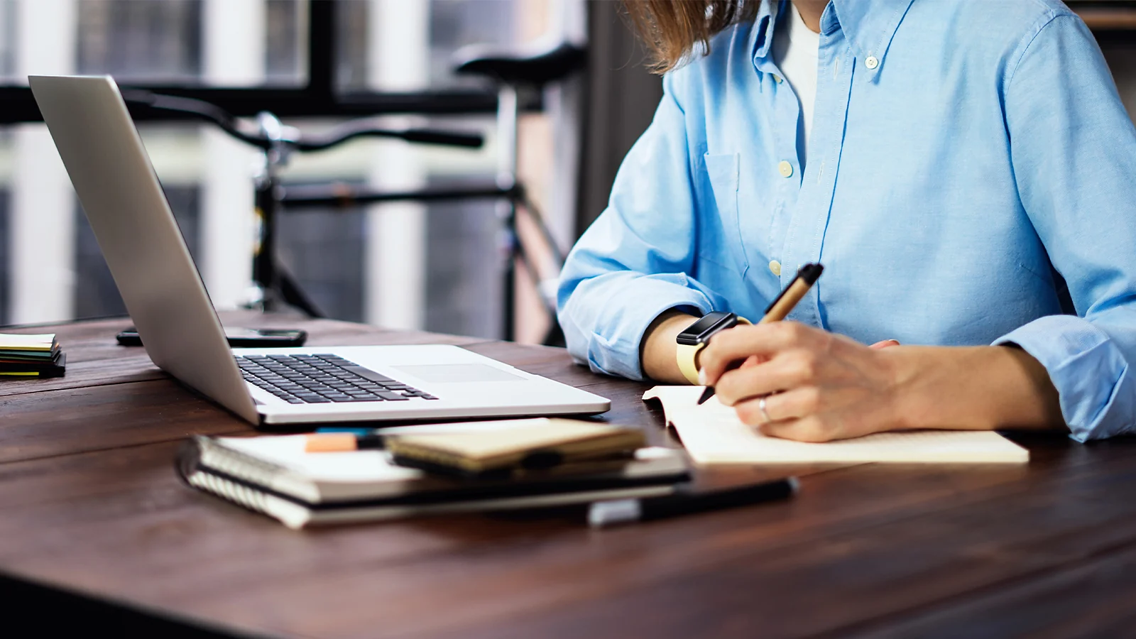 Writing in a notebook while working on a laptop, focused on blogging