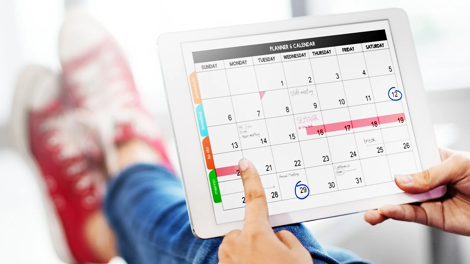 Hands holding a tablet showing a digital planner and calendar with various appointments and color-coded events
