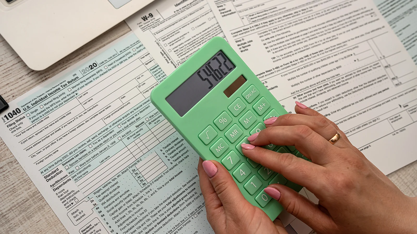 Close-up of hands using a green calculator over a 2020 IRS Form 1040 U.S. Individual Income Tax Return
