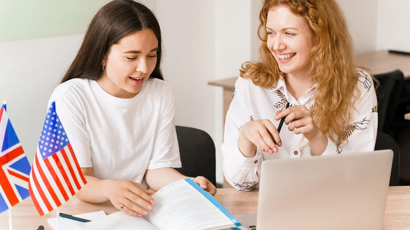 two women sitting next to the laptop