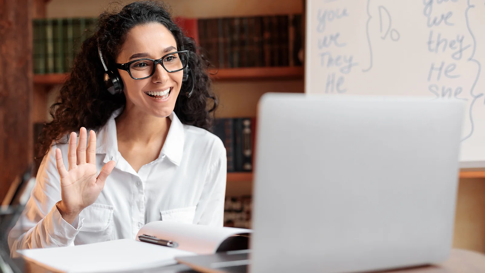 Online tutor wearing a headset and smiling while conducting a remote lesson on a laptop