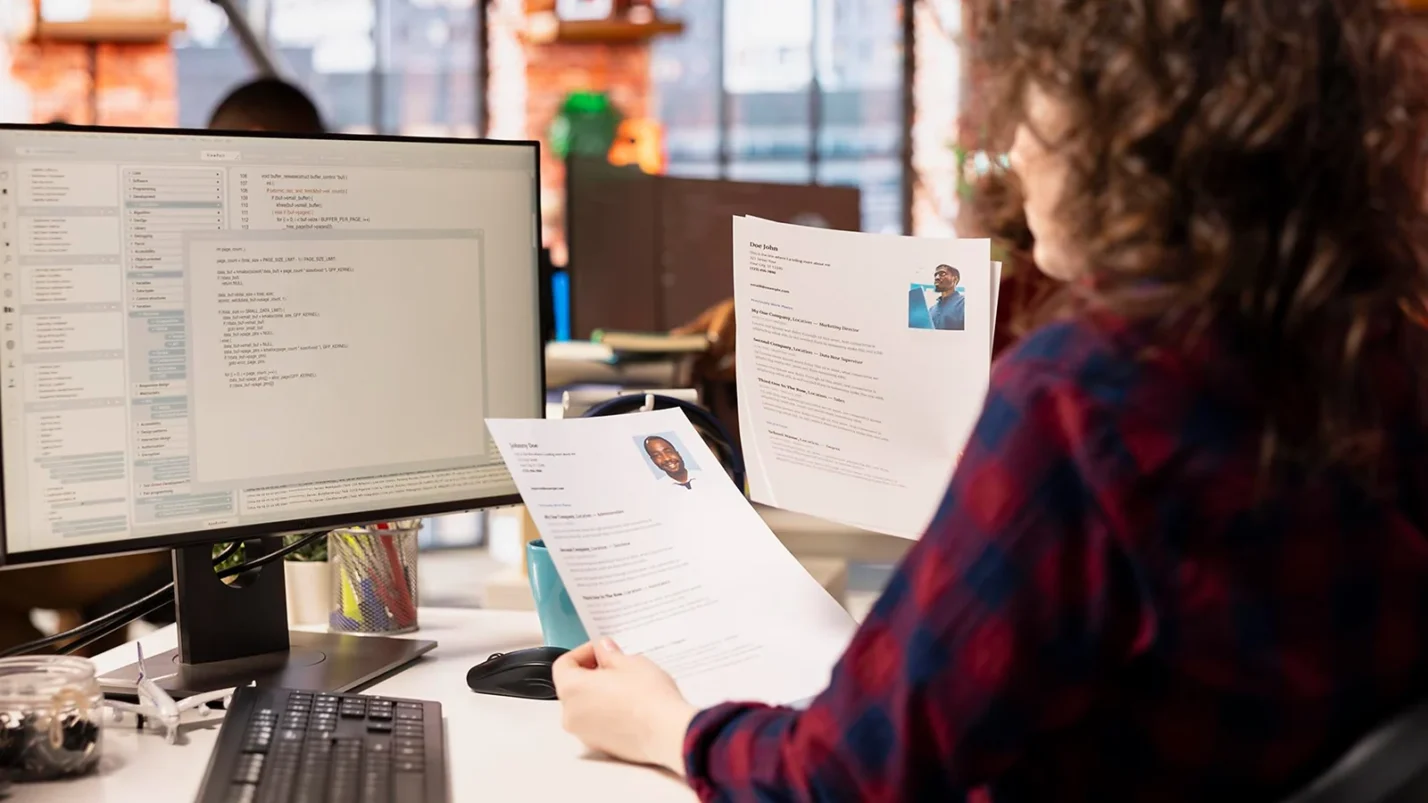 Woman looking at the laptop and holding CVs