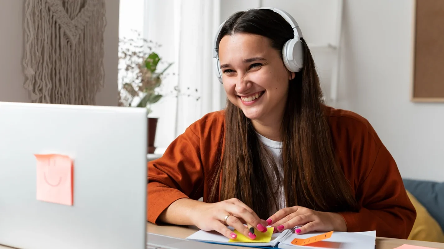 smiling woman sitting in front of laptop with headphones