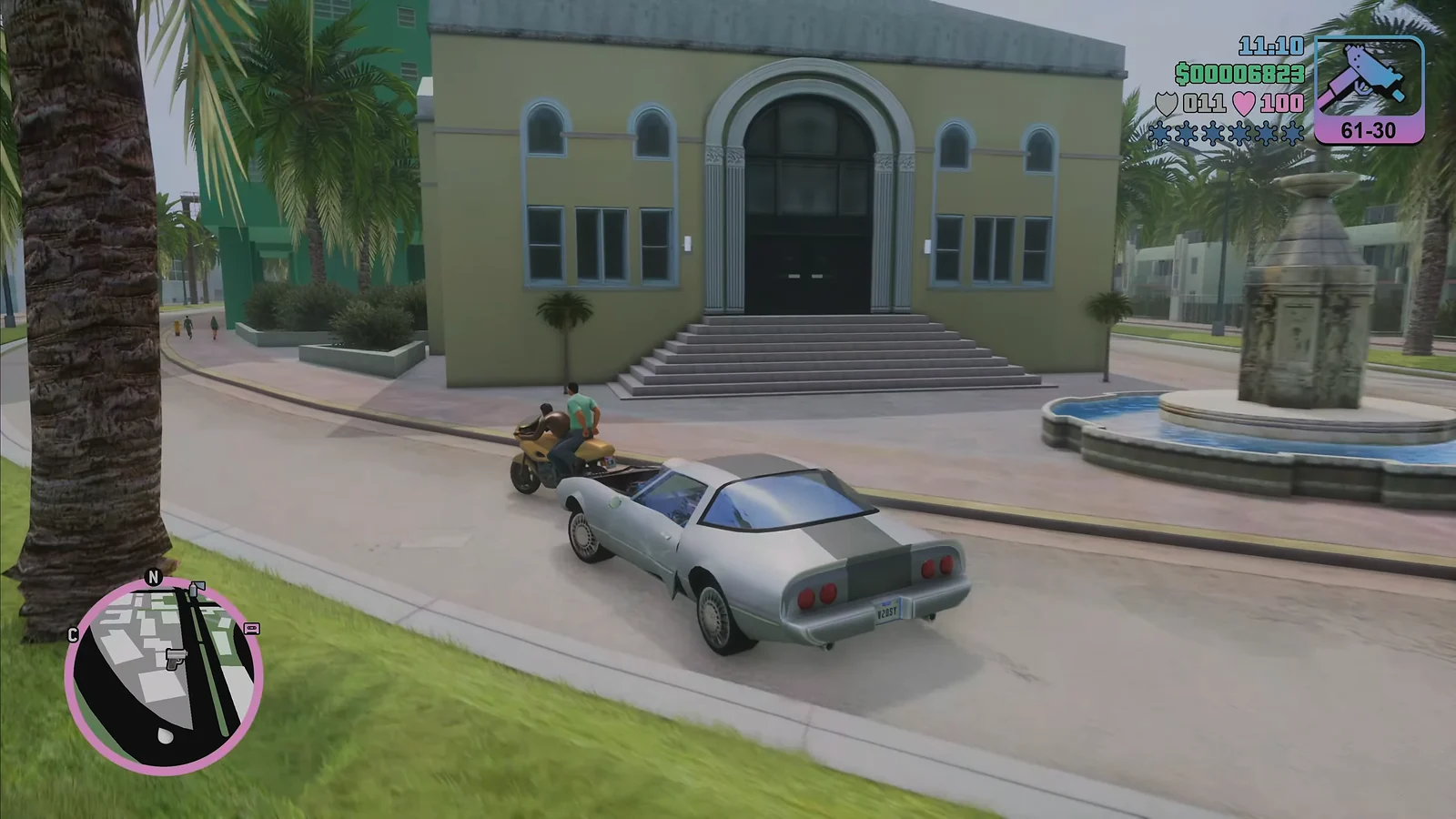 Tommy Vercetti driving a silver sports car past a fountain in Vice City
