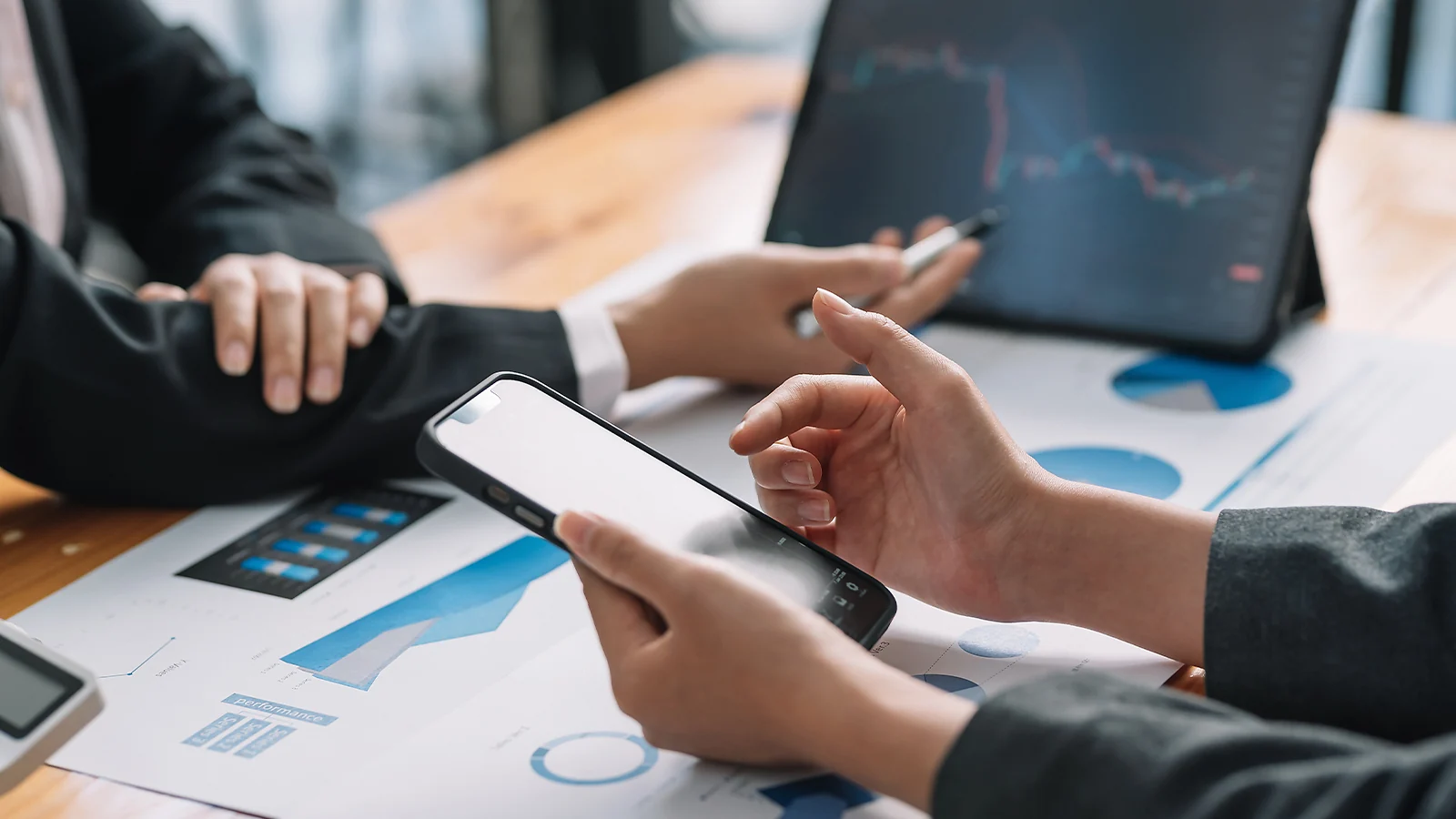 Análisis de resultados: unas manos que sostienen un smartphone sobre gráficos financieros y datos de mercado