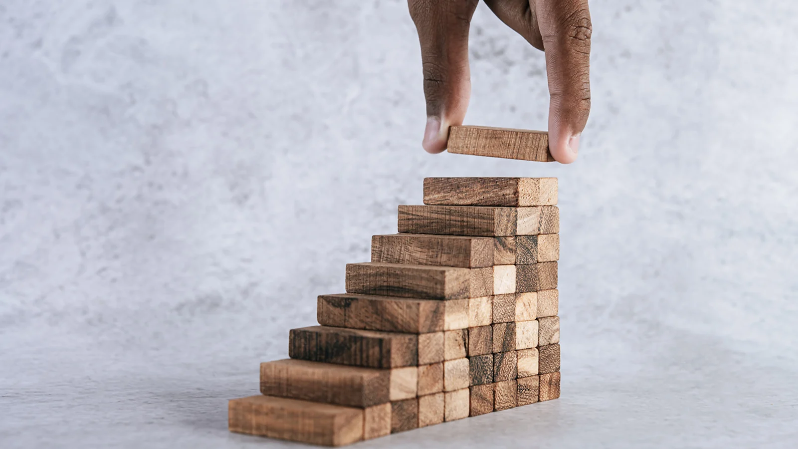 Eine Hand, die einen Holzklotz auf eine Treppe aus Holzwürfeln legt.