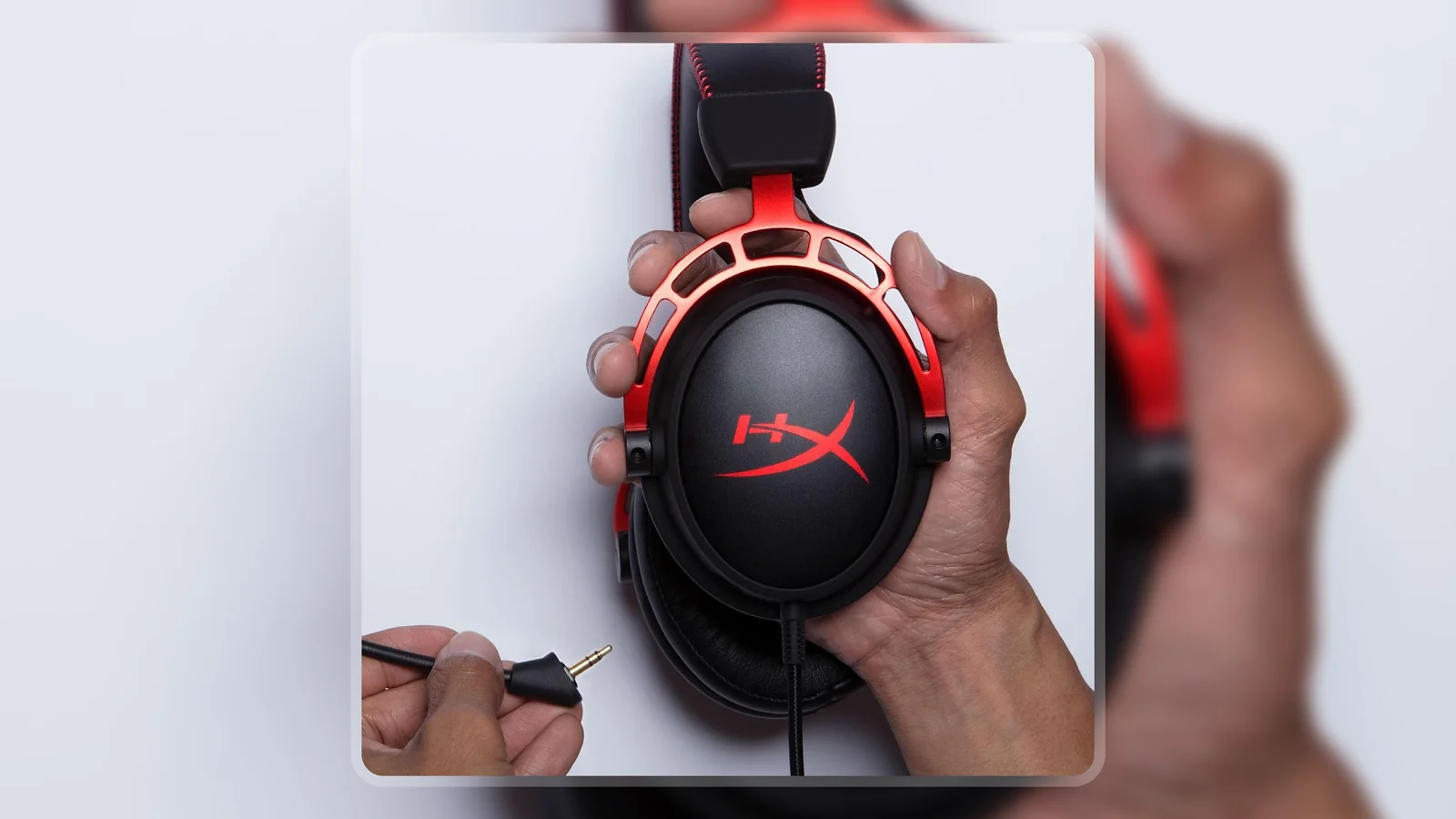 Hands holding the HyperX Cloud Alpha gaming headset while inserting the 3.5mm audio cable