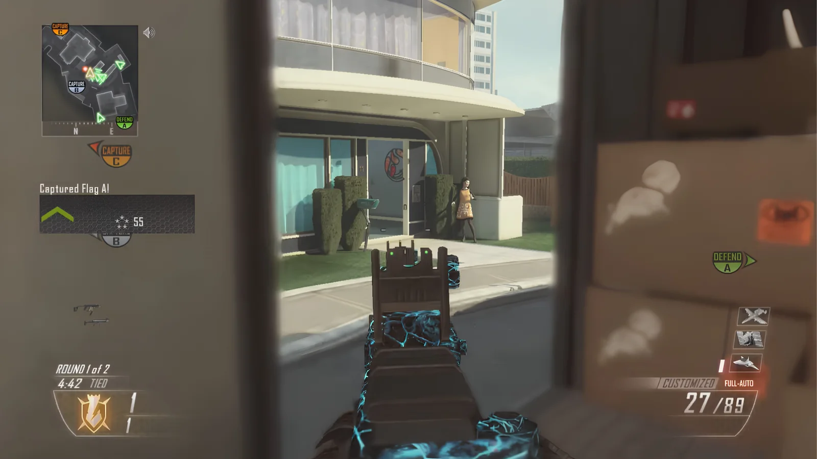 First-person perspective screenshot from Call of Duty: Black Ops II on the Nuketown 2025 map, aiming a weapon with a blue patterned camo toward a retro futuristic house.