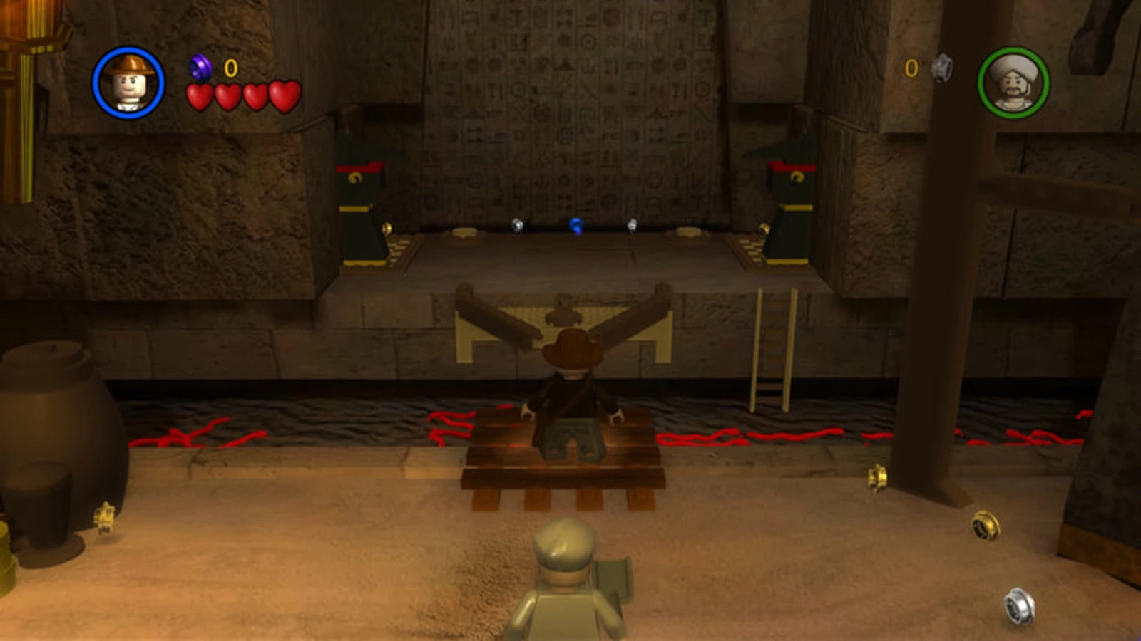 Indiana Jones stands on a wooden platform before an ancient temple wall covered in carved symbols
