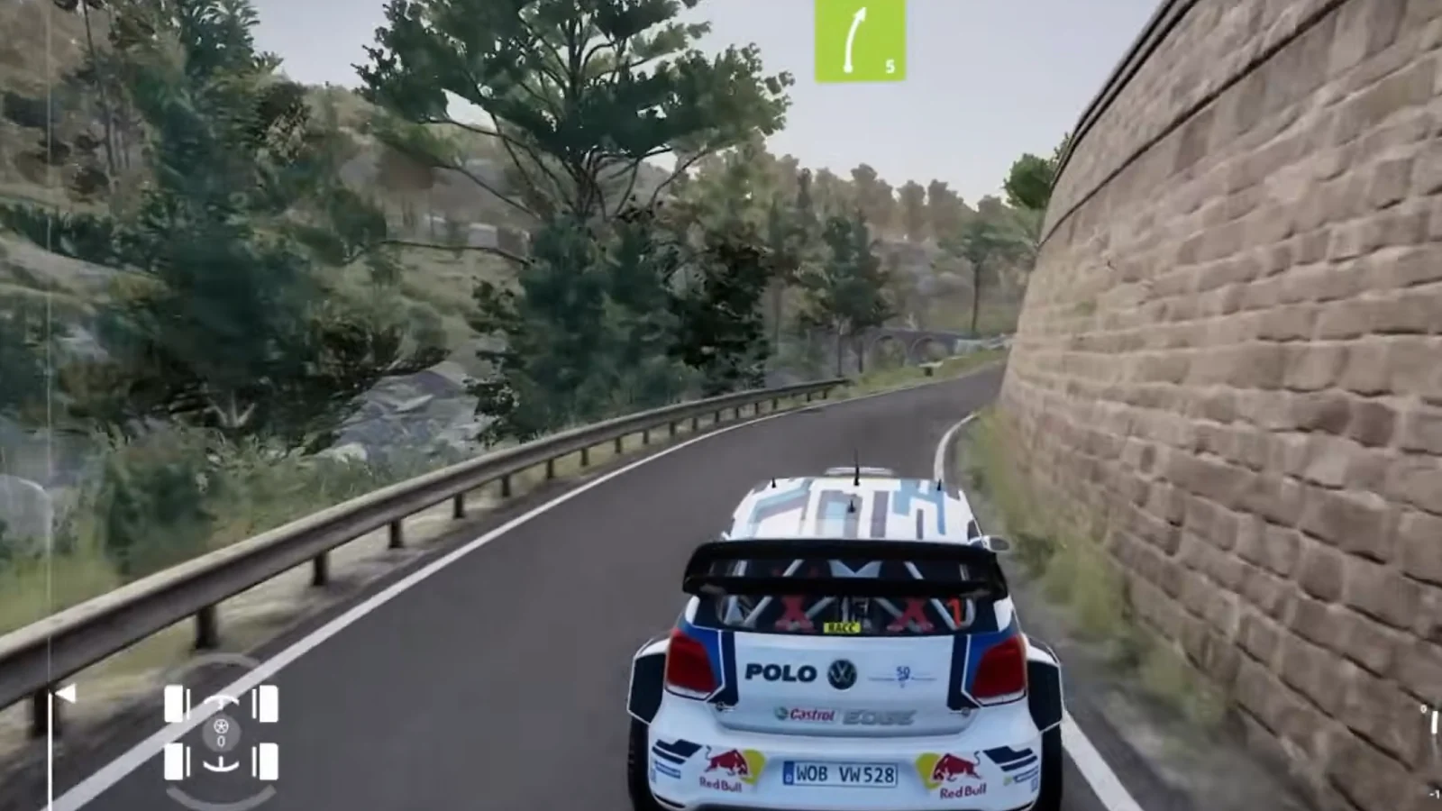 A rally car races along a narrow mountain road beside a stone wall.